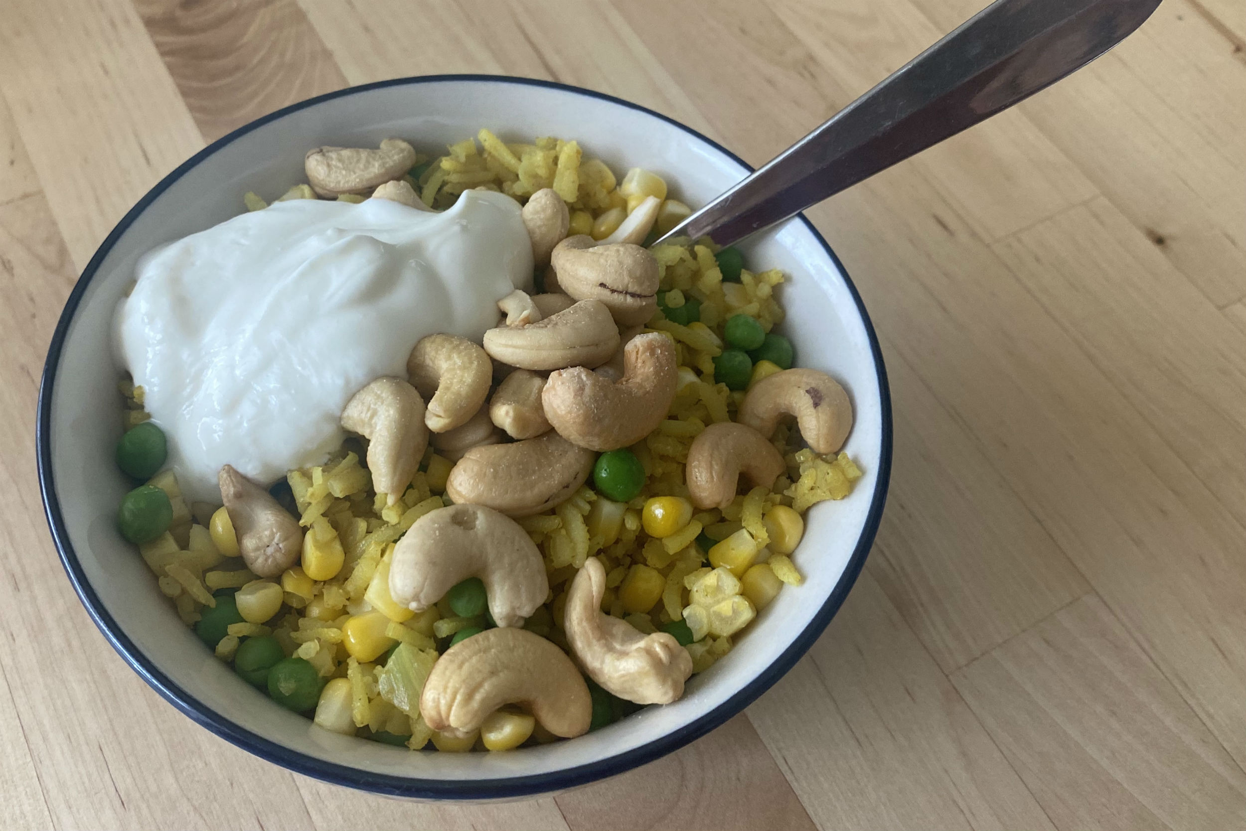 small bowl of yellow rice with cashews, peas, corn and yoghurt on top