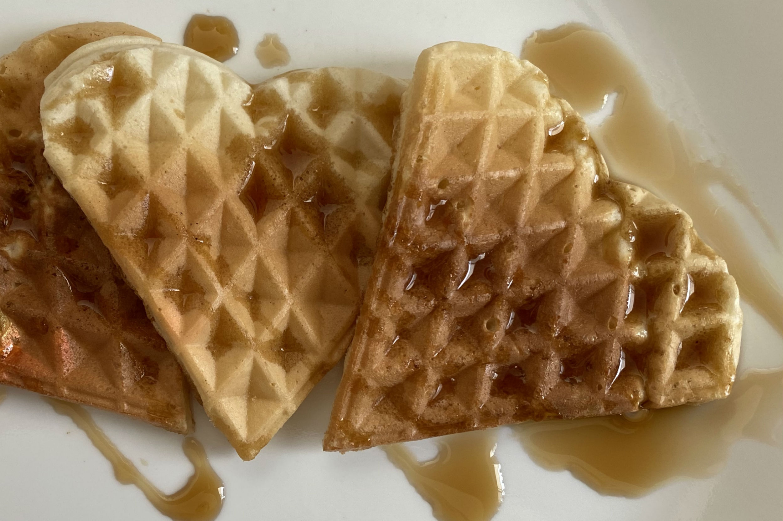 heart shaped waffles on plate drizzled with maple syrup