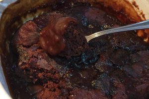 chocolate self-saucing pudding in oven dish with metal spoon